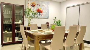 Un comedor con una mesa de madera, sillas blancas, un aparador de vidrio y un cuadro de flores.