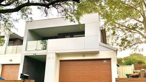 Una casa moderna de dos pisos con garaje, un espacio exterior cubierto y un pequeño jardín delantero.