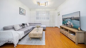 Ein modernes Wohnzimmer mit grauem Sofa, einem Holztisch und einem Flachbildfernseher, der einen Blick auf den Hafen von Sydney zeigt.