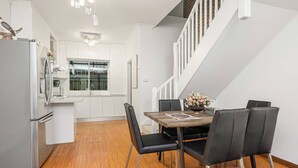 Eine moderne Küche mit weißen Schränken, einem Edelstahlkühlschrank und einem Holzespeisetisch mit schwarzen Stühlen.