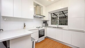 Eine moderne Küche mit weißen Schränken, einem Einbauofen, einer Mikrowelle und einem Fenster mit Blick ins Freie.