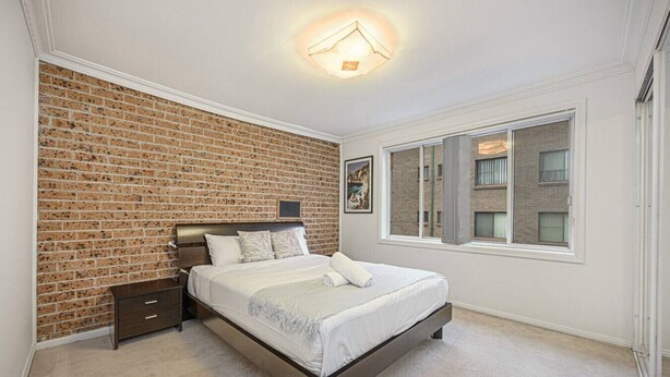 Ein Schlafzimmer mit Backsteinwand, großem Fenster und einem Bett mit weißer Bettwäsche.