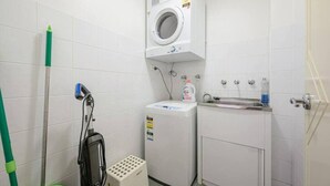 Une petite buanderie équipée d’un lave-linge, d’un sèche-linge, d’un évier et d’un balai.