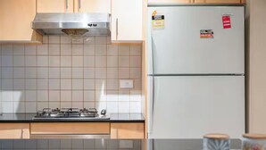 Une cuisine équipée d’une cuisinière à gaz, d’une hotte en acier inoxydable, d’un réfrigérateur blanc et d’un dosseret carrelé.
