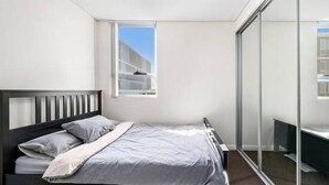 A bedroom with a bed, a window, and a sliding glass door leading to a balcony. - 2BR APT near Train Station/4ppl/Couple/Business (Canterbury)