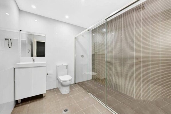 Un baño moderno con inodoro, lavamanos y cabina de ducha con mampara de vidrio.