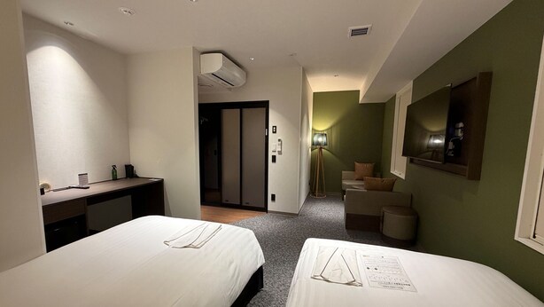 Ein Hotelzimmer mit zwei Betten, einem Schreibtisch, einem Spiegel und einer kleinen Sitzecke.