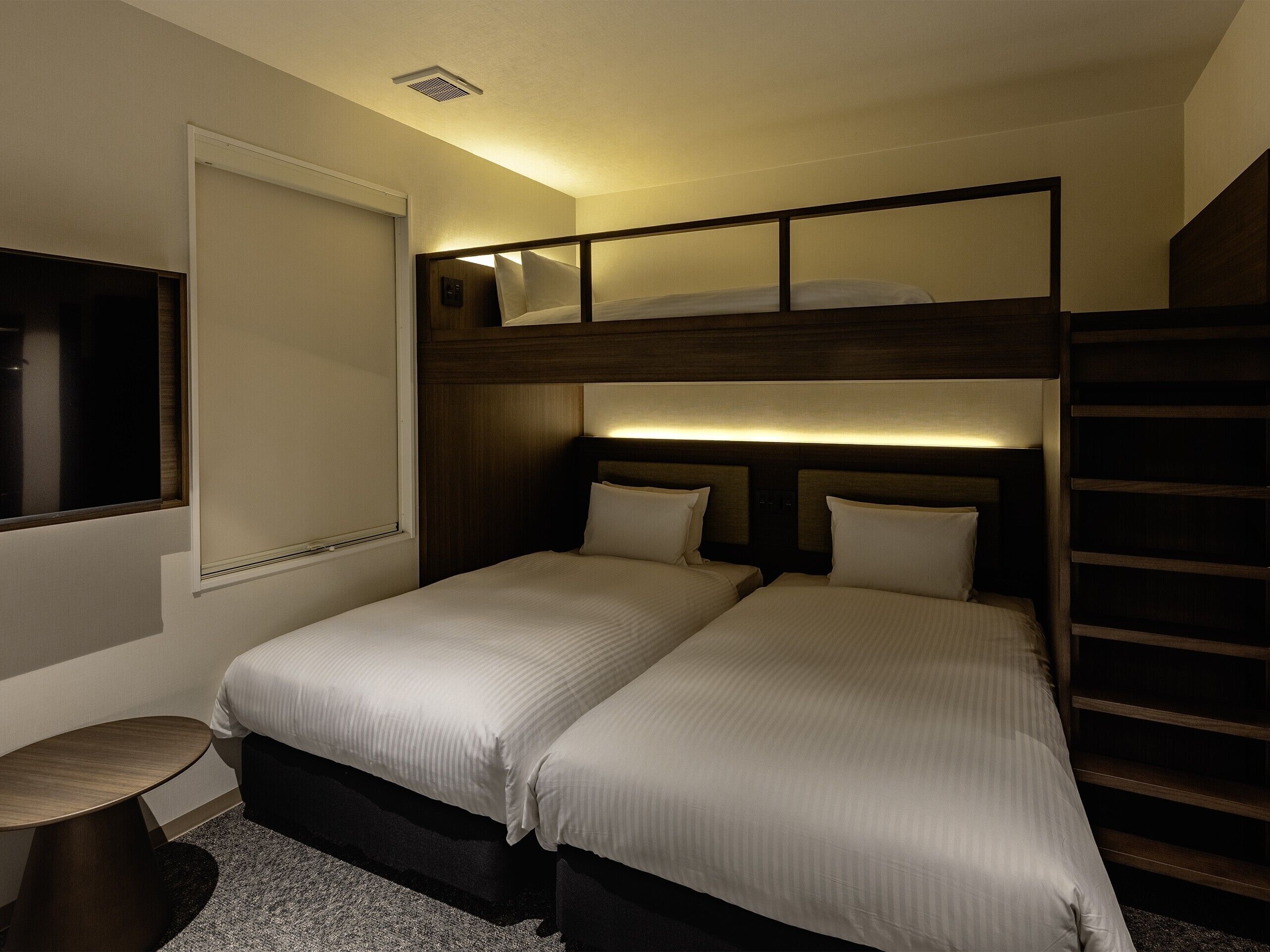 A hotel room with a bunk bed, a bedside table, and a small round table.