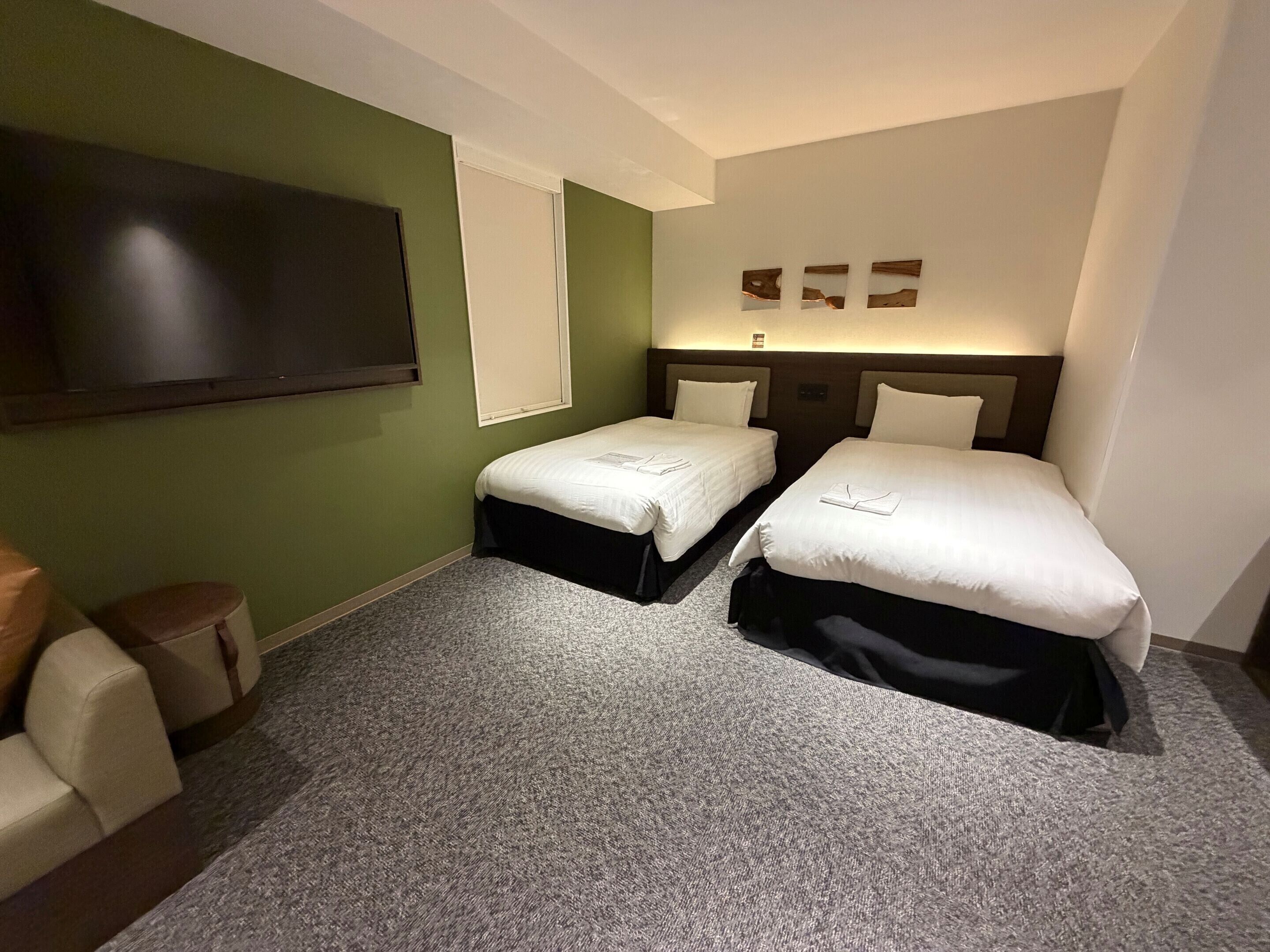 Habitación de hotel con dos camas, televisión de pantalla plana, ventana y una obra de arte colgada en la pared.