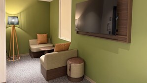 Ein Zimmer mit einem großen Flachbildfernseher an der Wand, einer Stehlampe und zwei Sofas mit Kissen.