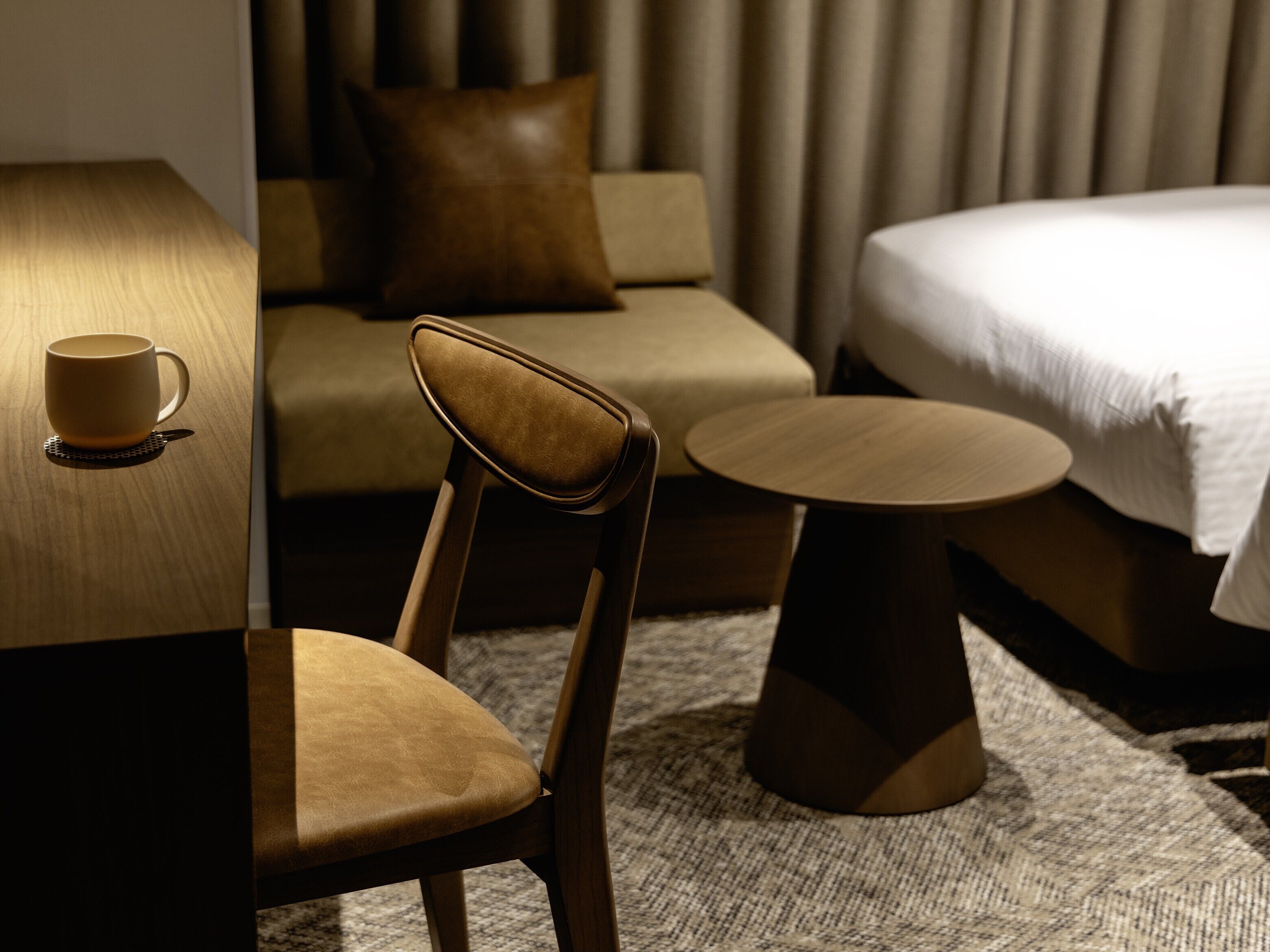 A hotel room with a bed, a sofa, a chair, a small table, and a cup on a coaster.
