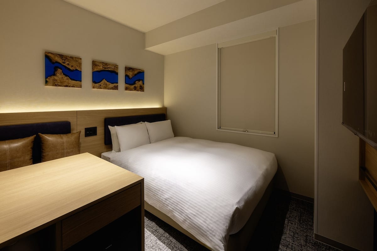 Una habitación de hotel con cama, escritorio y dos cuadros colgados en la pared.