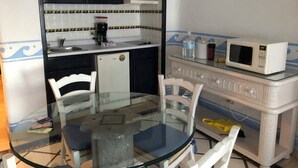 Cocina compacta con refrigerador, microondas y cafetera. Hay una mesa de vidrio con sillas y una pequeña encimera.
