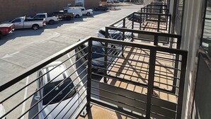 Un espace extérieur abrité, doté d’une rambarde en métal, un parking et un bâtiment à la façade en pierre.