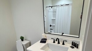 Une salle de bain moderne avec un lavabo blanc, des meubles de rangement aux couleurs foncées et un grand miroir au-dessus du meuble-lavabo.