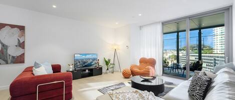 A modern living room with a flat-screen TV, red and white sofas, a coffee table, and a large window with a city view.