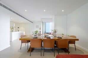 A modern dining area with a long wooden table, six chairs, and a kitchen in the background. - Waterfront CBD luxury 3Br  with Parking for 8 ppl (Barangaroo)