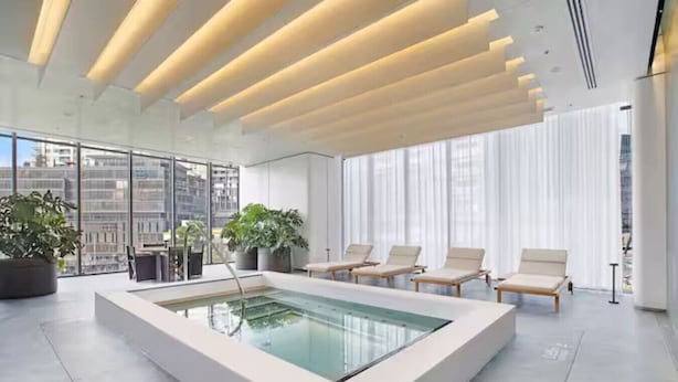 Een modern binnenzwembad met glazen wanden, lounge fauteuils en potplanten.