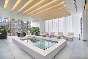 Een modern binnenzwembad met glazen wanden, lounge fauteuils en potplanten.