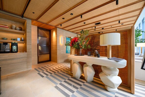 Een moderne hotellobby met een receptiebalie, een koffieapparaat en een decoratieve vaas met bloemen.