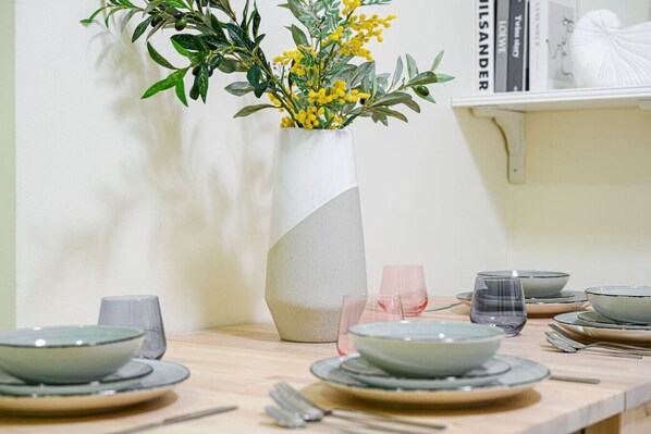 A dining table set with plates, bowls, and cutlery, accompanied by a vase with yellow flowers. - CBD 3br apt for 8 guests near Train & Shopping (Ultimo)
