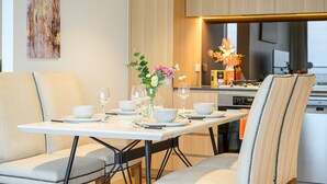A dining area with a table set for four, chairs, a vase with flowers, and a kitchen in the background. - Parramatta 2br Apt Near Train Shopping Center (Parramatta)
