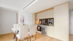 A modern kitchen with wooden cabinets, a dining area with white chairs, and a small table. - Parramatta 2br Apt Near Train Shopping Center (Parramatta)