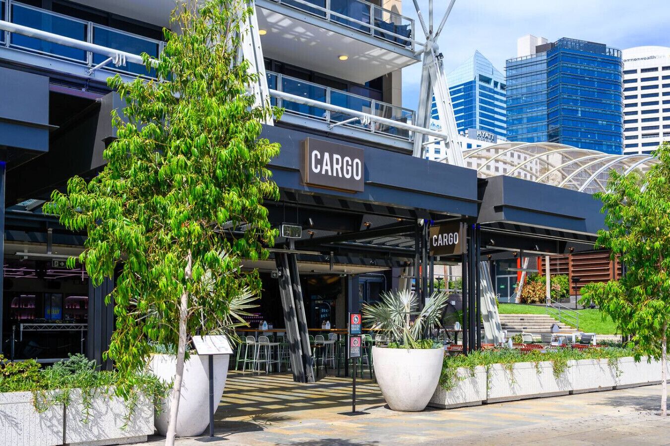 A modern building with a 'CARGO' sign, surrounded by greenery and urban architecture.