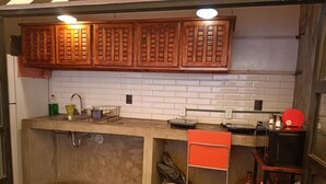 A kitchen with wooden cabinets, a white tiled backsplash, a sink with a dish rack, and a red chair.