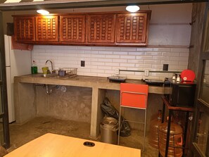 Eine Küche mit Holzschränken, einer weißen Fliesenspiegel, einer Spüle mit Geschirrständer und einem roten Stuhl.