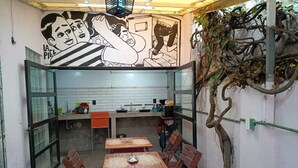 A small outdoor dining area with a tiled floor, wooden tables and chairs, and a mural on the wall.