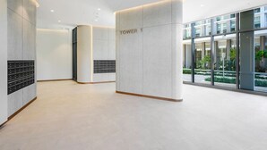 Un moderno vestíbulo de hotel con diseño minimalista, que incluye un mostrador de recepción con la leyenda "TOWER 1" y una pared de vidrio que ofrece vistas al área exterior.