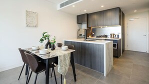 Una cocina moderna con una isla central, armarios oscuros y un comedor con una mesa preparada para dos.