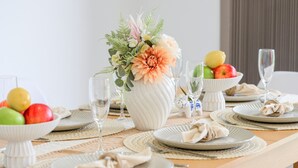 Ein Esstisch ist gedeckt mit Tellern, Fruchtschalen, einer Blumenvase und Weingläsern.