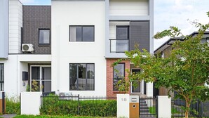 Ein modernes Reihenhaus mit weißer Fassade, Ziegeldetails und einem schwarzen Metallzaun.