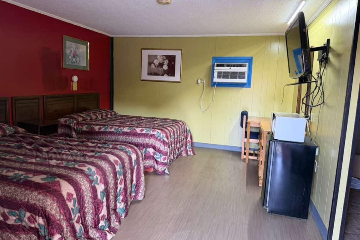 A room with two beds, a desk, a chair, a television, and an air conditioning unit.