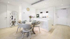 A modern kitchen with white cabinetry, a central island, and a dining area with a round table and chairs. - Waterfront CBD luxury 1Br with best view (Barangaroo)