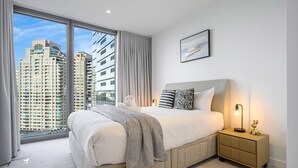 A modern bedroom with a large bed, a nightstand, and a view of tall buildings. - Waterfront CBD luxury 1Br with best view (Barangaroo)