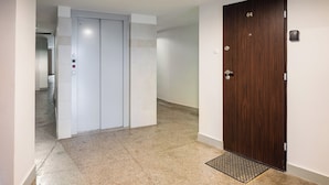 A hallway with a white elevator, a wooden door labeled '64', and a metal mat at the entrance. - Solec Powiśle Homely Apartment (Warszawa)