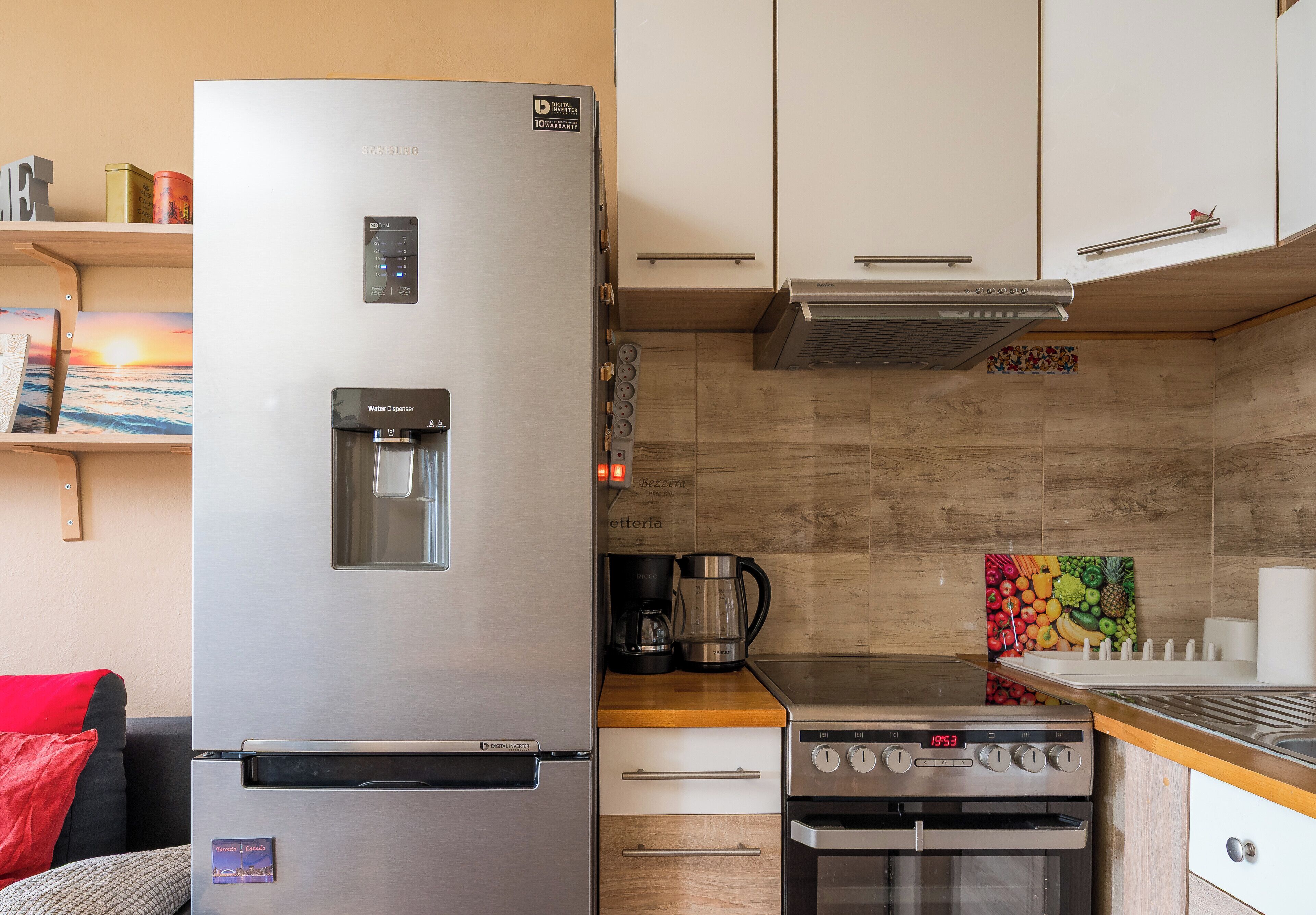 A compact kitchen with a stainless steel refrigerator, a water dispenser, a coffee maker, a stove, and a microwave.