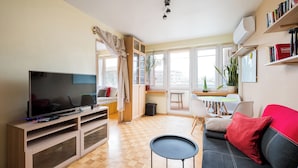 A living room with a flat-screen TV, wooden flooring, a red sofa, a small round table, and a bookshelf. - Solec Powiśle Homely Apartment (Warszawa)