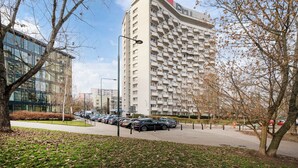 A modern high-rise building with multiple balconies, a parking area with cars, and a clear sky. - Solec Powiśle Homely Apartment (Warszawa)