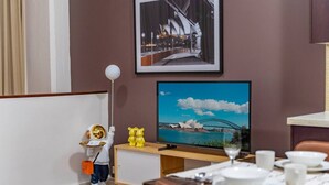 Een hotelkamer met een eethoek, een televisietoestel waarop een mooi uitzicht te zien is, een lamp in de vorm van een beer en een beerbeeldje op het aanrecht.
