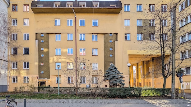 Ein mehrgeschossiges Wohngebäude mit flacher Fassade, zahlreichen Fenstern und einem zentralen Eingang.