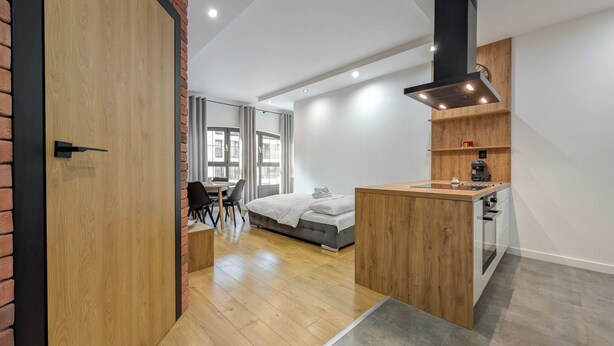 Habitación de hotel moderna con puerta de madera, una cama, un escritorio y una kitchenette.