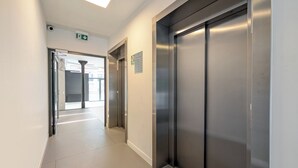 Un pasillo moderno con dos ascensores, una señal de salida visible y un piso de baldosas impecable.