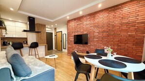 Una sala de estar moderna con un sofá azul, una mesa de comedor con sillas y una cocina con un televisor montado en una pared de ladrillo.