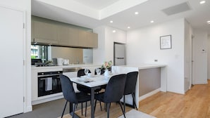 A modern kitchen with white cabinetry, a dining area with a white table and black chairs, and a small island with a sink. - Rosebery near Airport & Train & Shops (Rosebery)