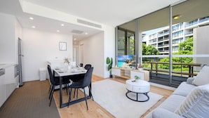 A modern apartment with a dining area, kitchen, and a balcony with a city view. - Rosebery near Airport & Train & Shops (Rosebery)