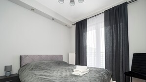 A modern bedroom with a large bed, a bedside table with a lamp, a chair, and a window with curtains. - Częstochowska Urban Comfort Apartment (Łódź)